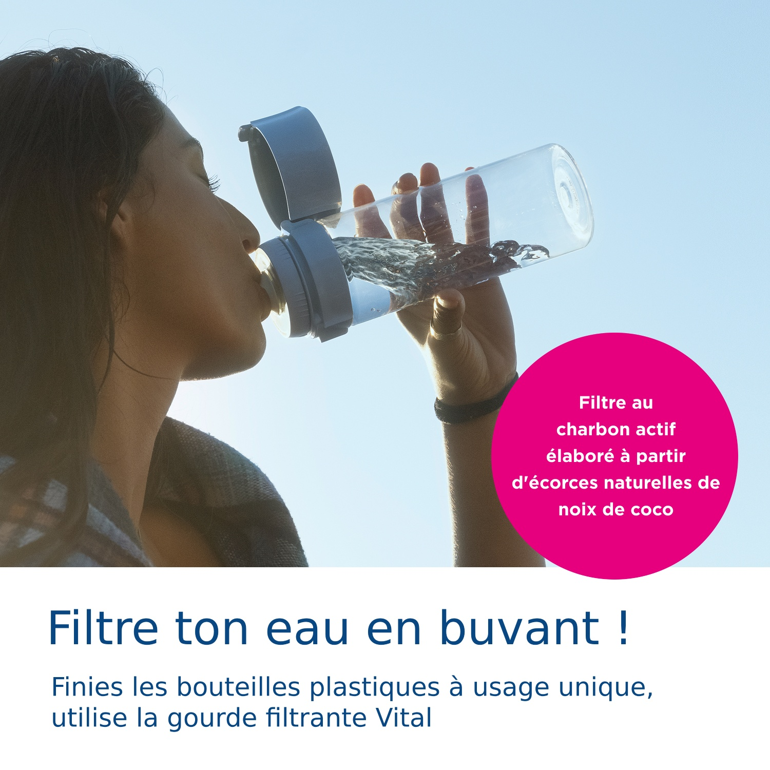 Een vrouw drinkt uit een transparante gefilterde waterfles tegen een helderblauwe lucht.