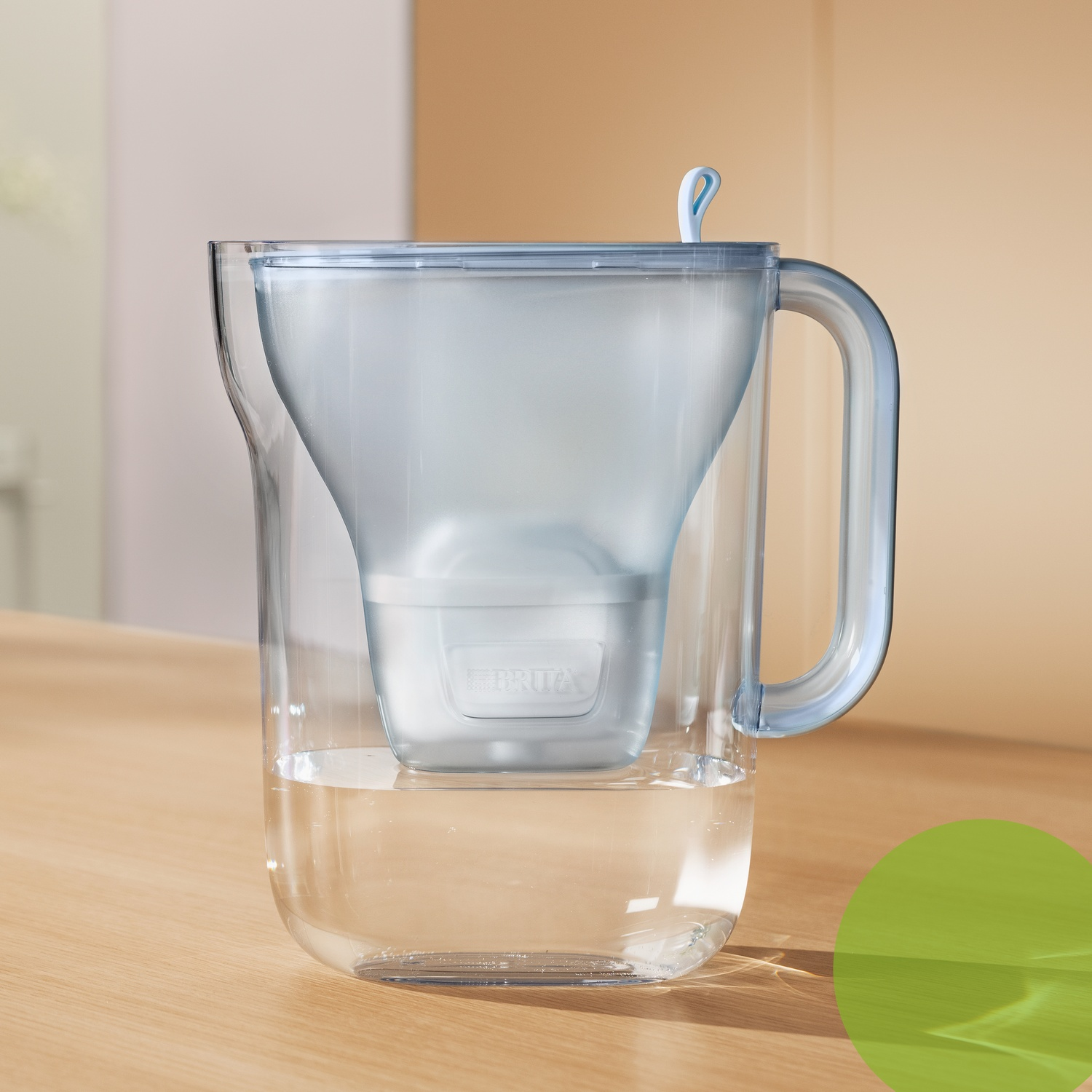 Een doorzichtige waterfilterkan met een blauw handvat en deksel staat op een houten tafel.