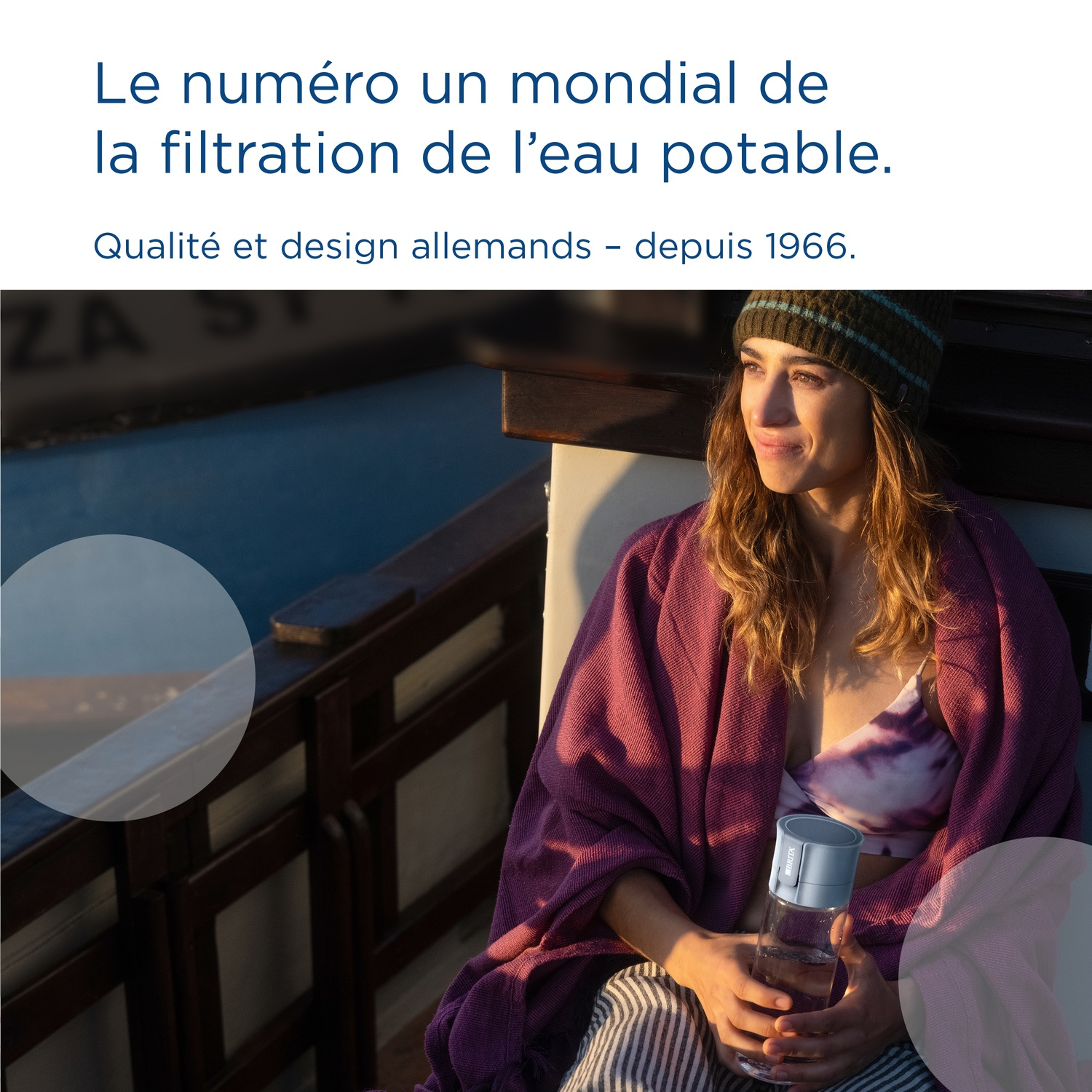 Een vrouw met muts en deken houdt een waterfles vast.