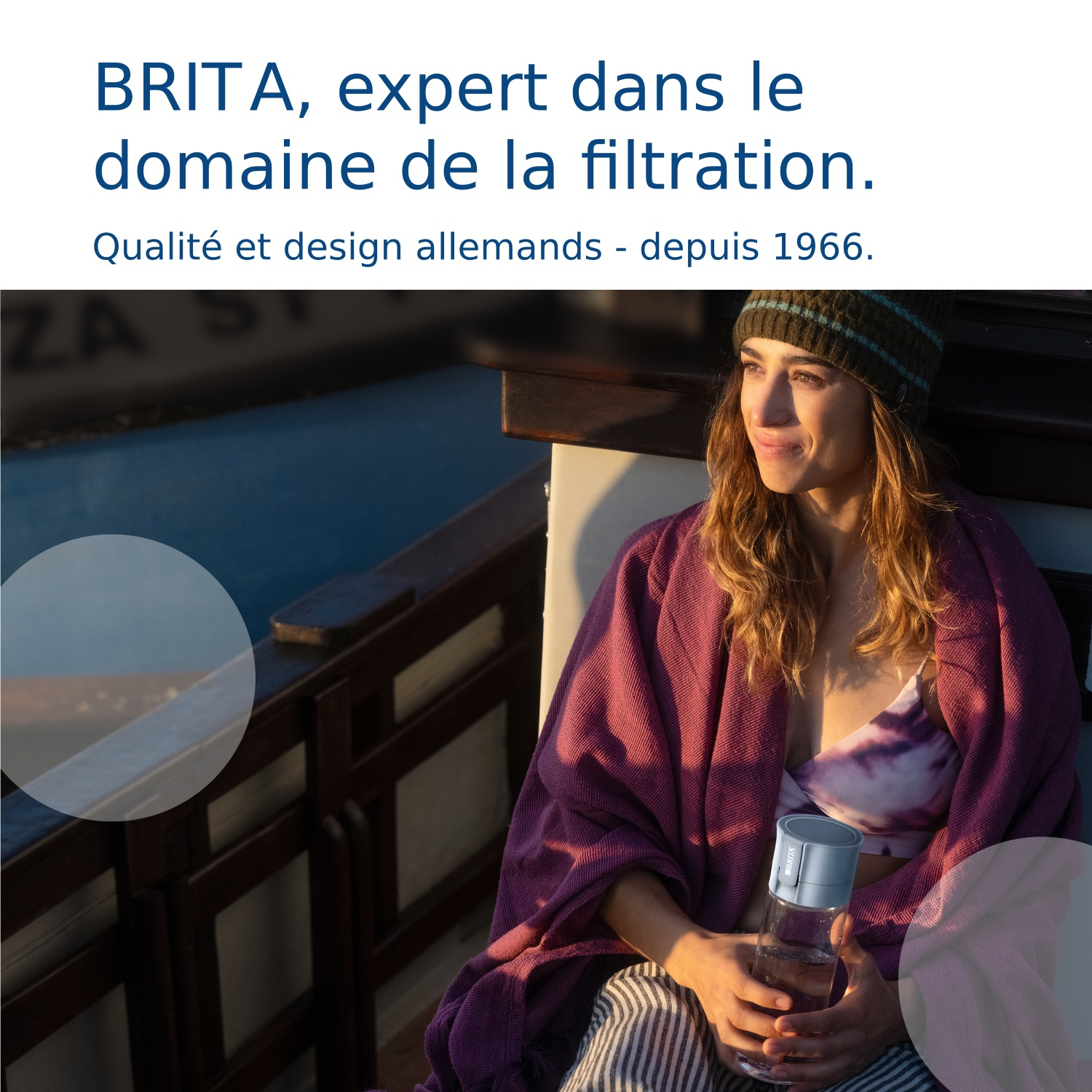 Een vrouw zit buiten, gewikkeld in een deken, en houdt een Brita-fles vast.