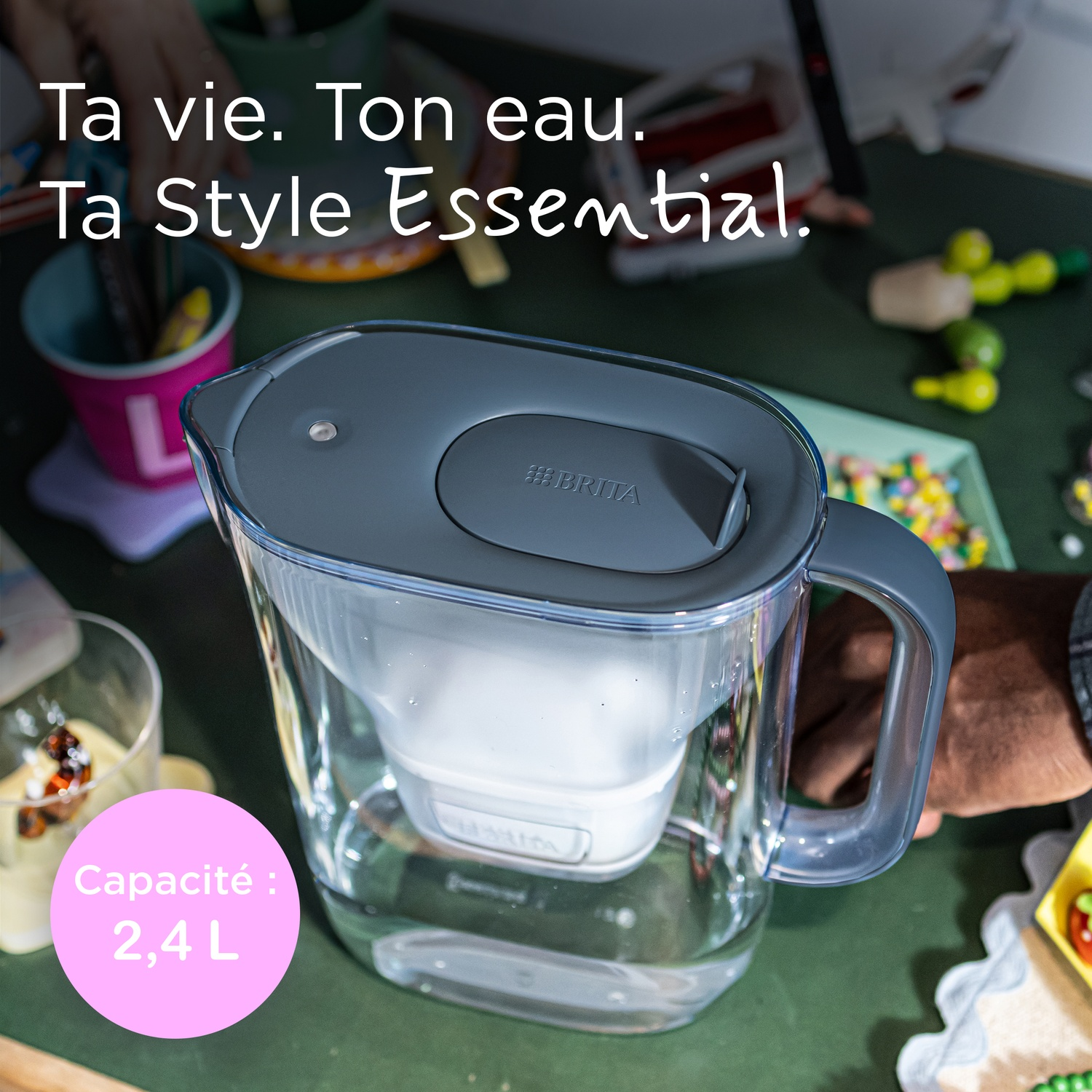 Une carafe Brita avec filtre à eau est sur une table, avec un verre et des jouets.