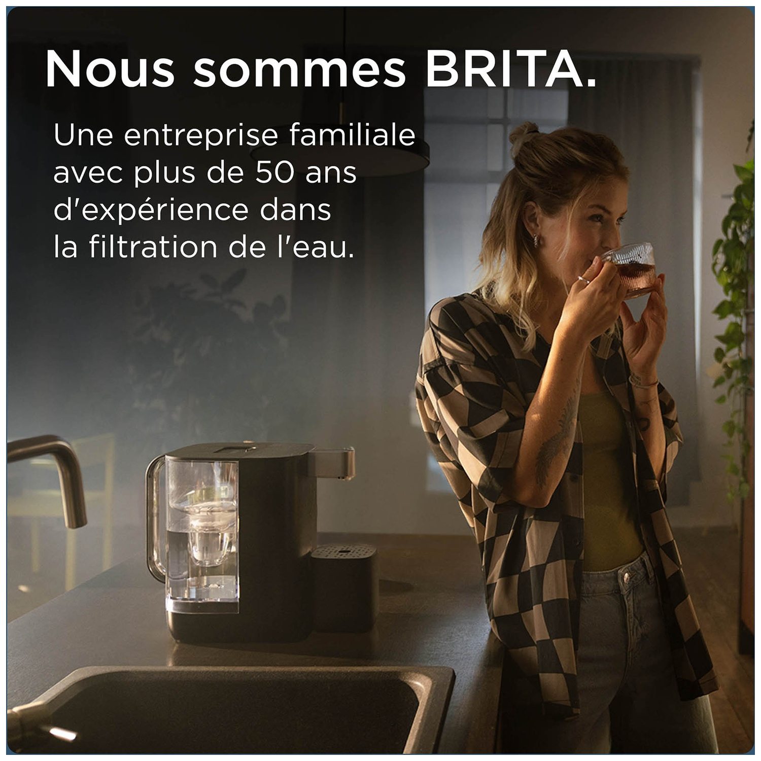 A woman drinks water from a glass next to a BRITA water filter on a kitchen counter.