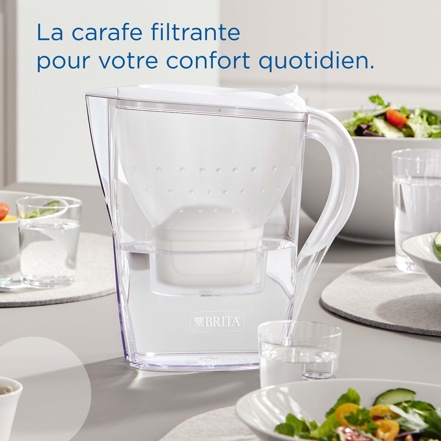 Een doorzichtige Brita filterkan staat op een tafel met saladekommen en glazen.