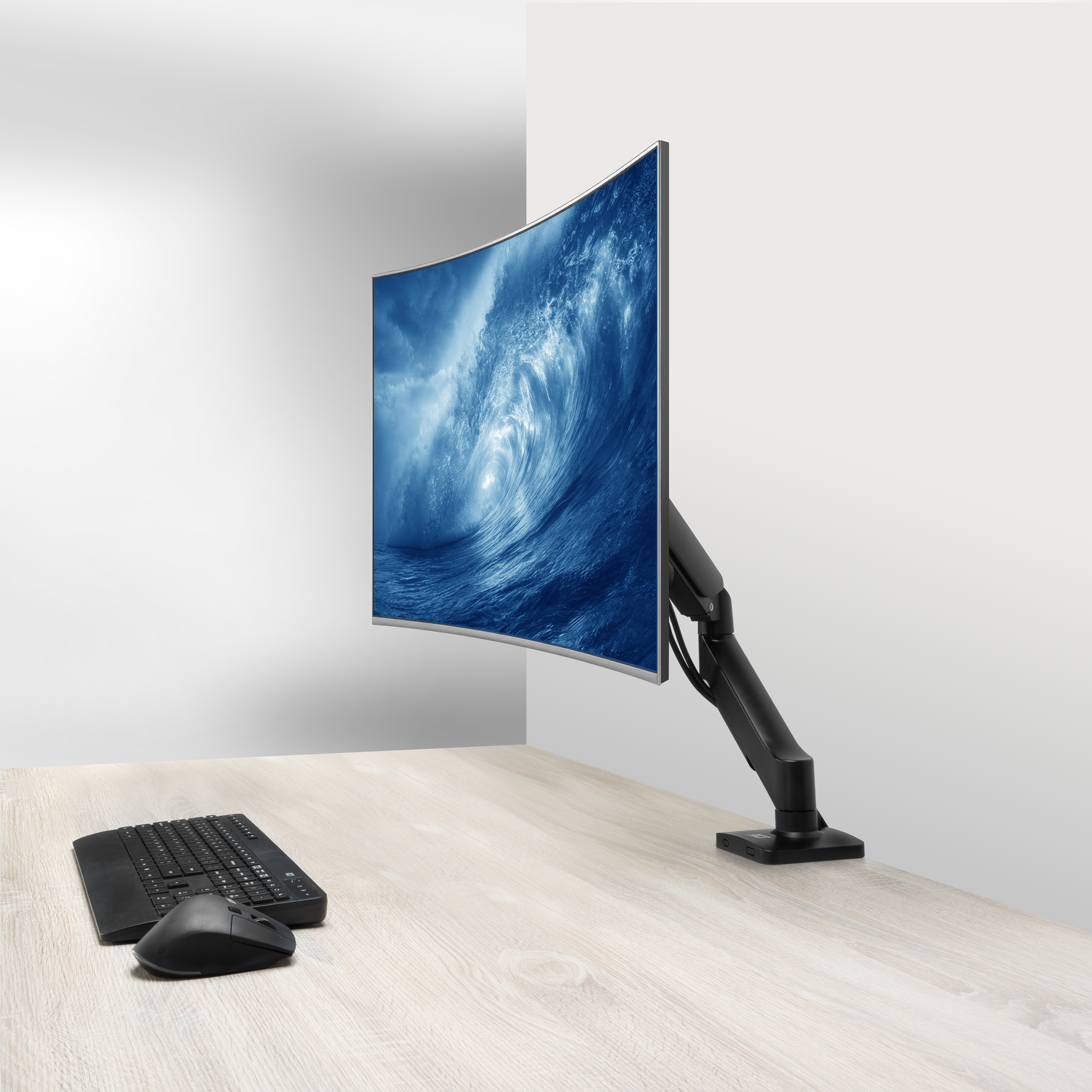 A curved monitor displaying a wave screensaver, with a keyboard and mouse on a wooden desk.