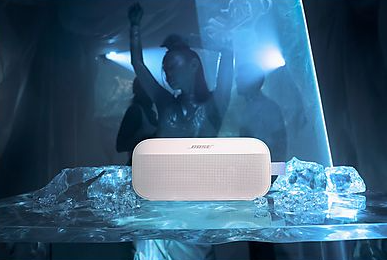 Biały głośnik Bose na lodzie. Sylwetki tańczą w niebieskim świetle w tle.