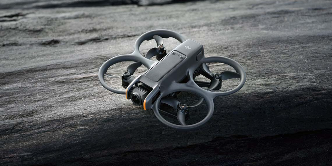 Szara dron z wirnikami spoczywa na ciemnej, teksturowanej powierzchni.