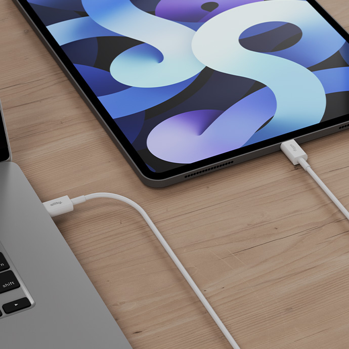 Egy laptop és egy tablet fehér kábelekkel van összekötve egy faasztalon.
