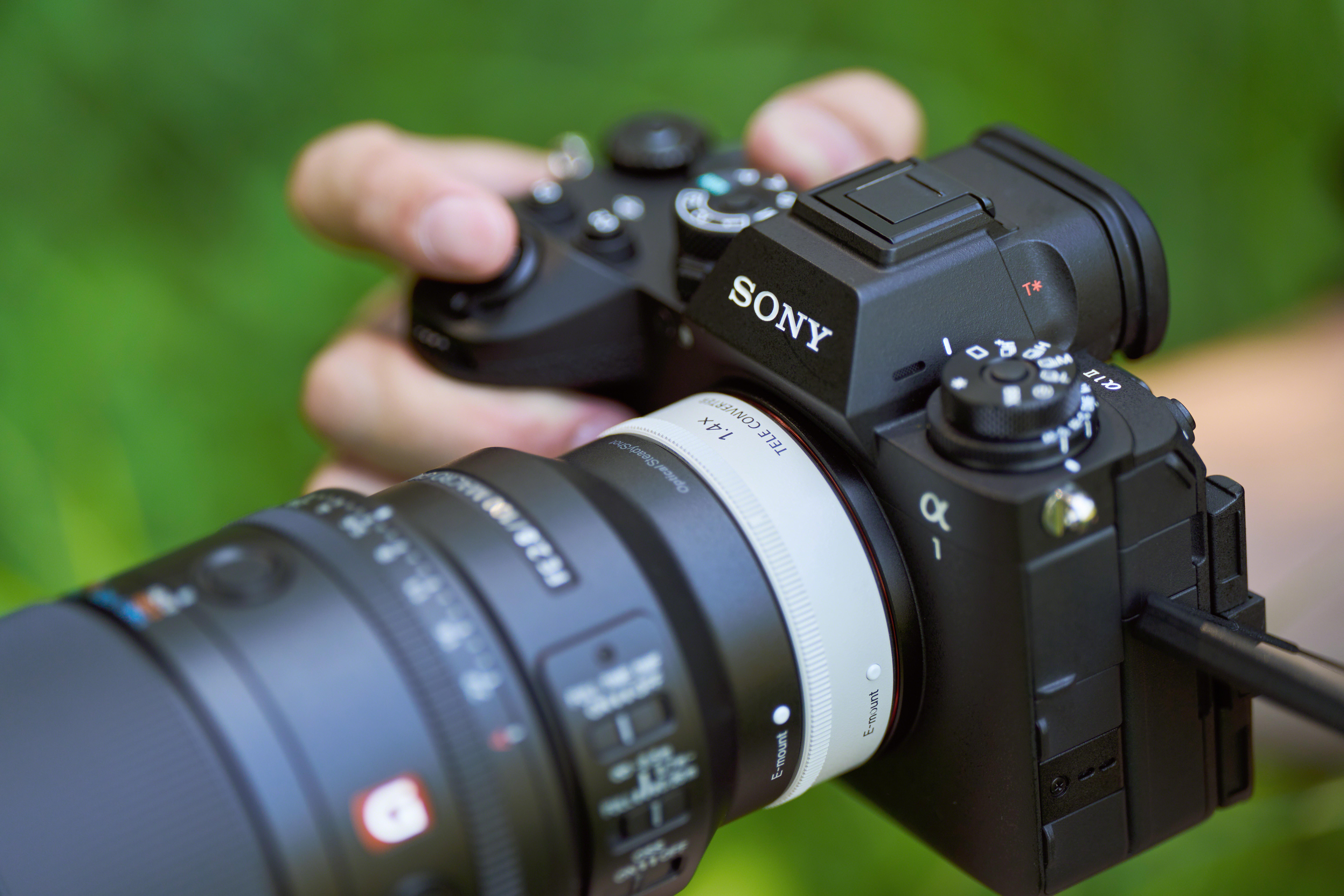 Eine Hand hält eine Sony-Kamera mit einem Telekonverter und einem Objektiv.