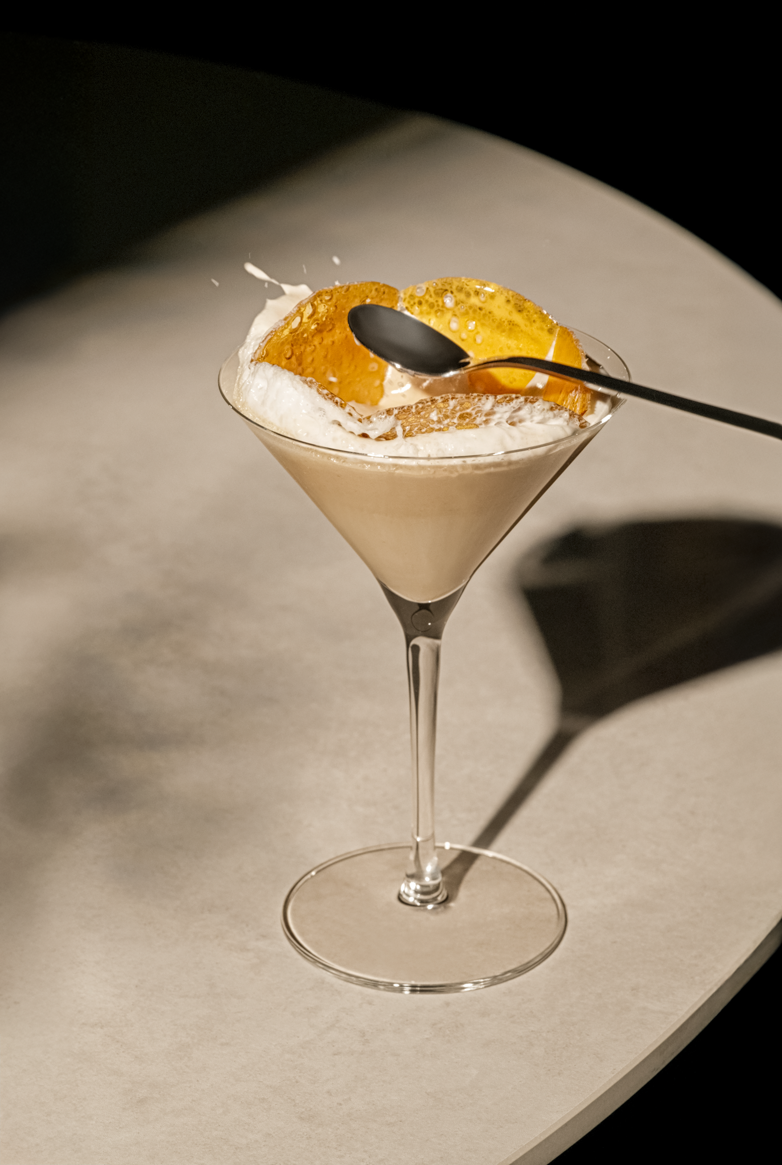 Ein Martini-Glas mit braunem Getränk, Sahne und Orangenscheibe, Löffel darin.