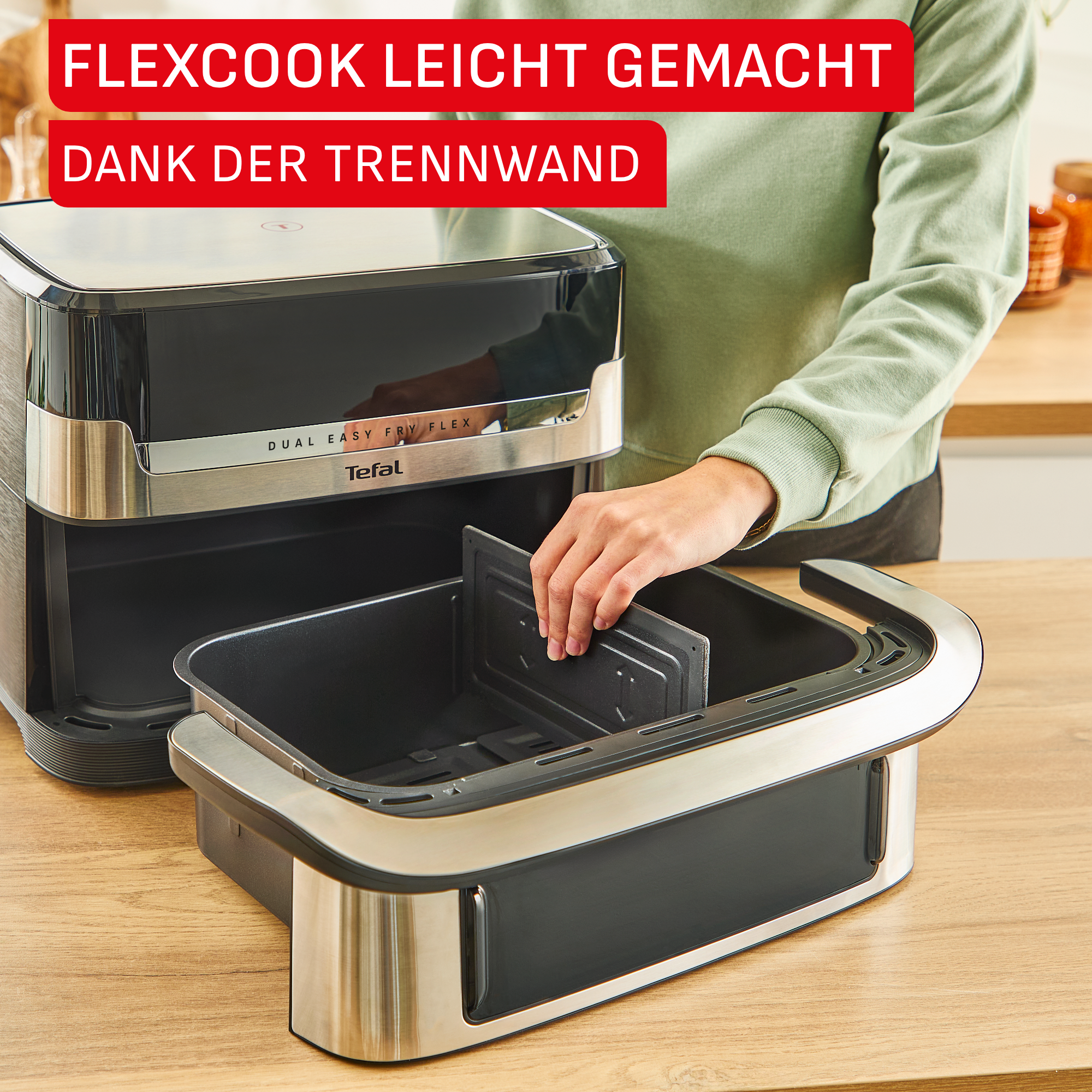Eine Person setzt eine Trennwand in einen schwarzen Heißluftfritteusen-Einsatz ein.