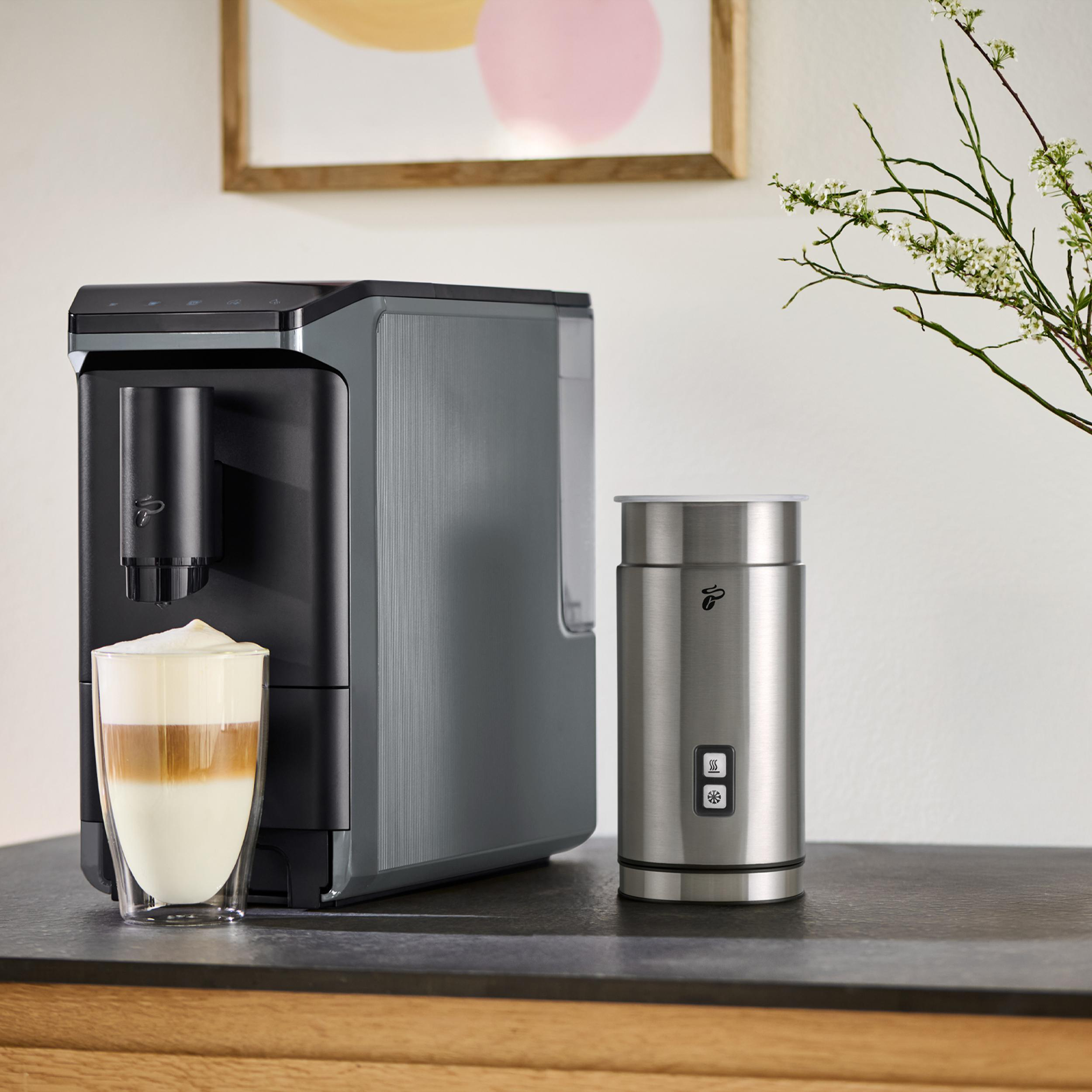 Kaffeemaschine mit Milchschaumbehälter und einem Latte Macchiato Glas daneben.