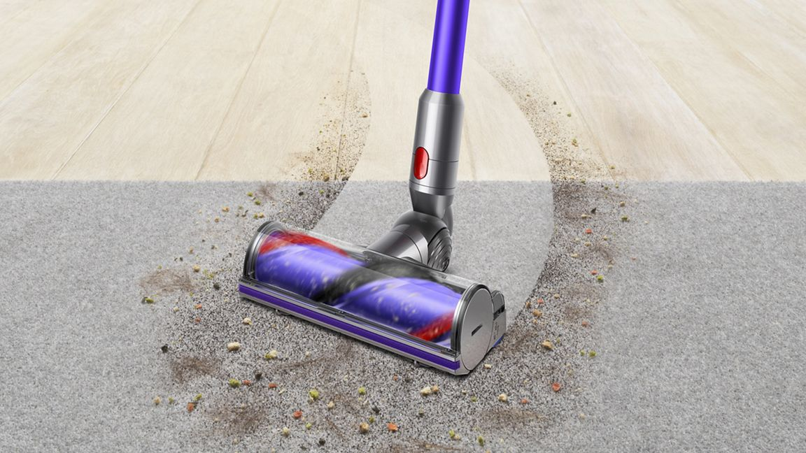 Una aspiradora morada limpia la suciedad de alfombra y suelo de madera.