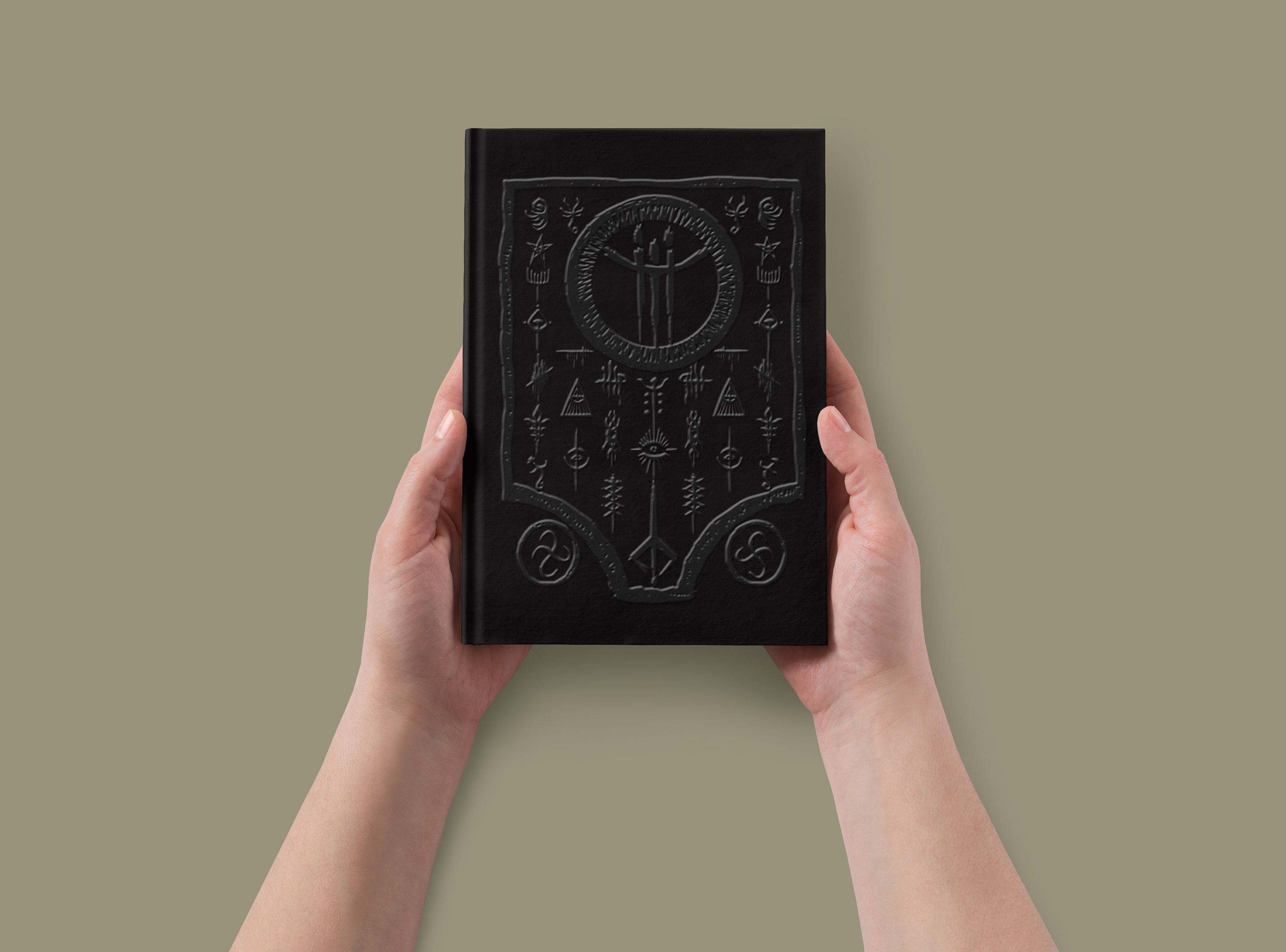 Manos sostienen un libro negro con símbolos en relieve sobre fondo liso.