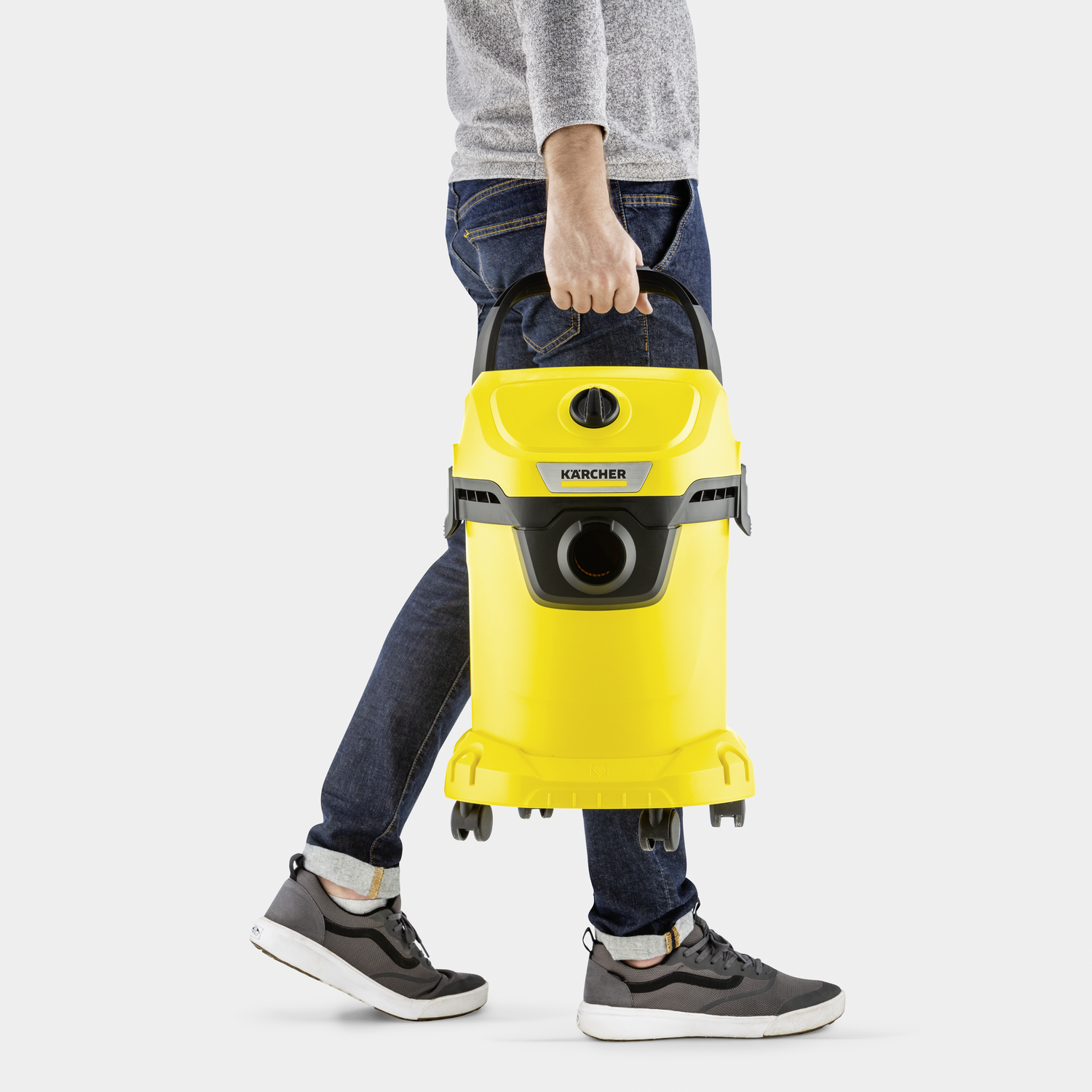Man carries yellow Kärcher wet/dry vacuum with black handle.