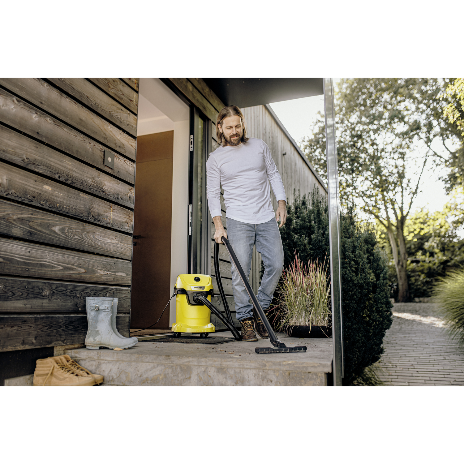 Man vacuums steps with yellow Karcher vacuum. Rubber boots and shoes nearby.
