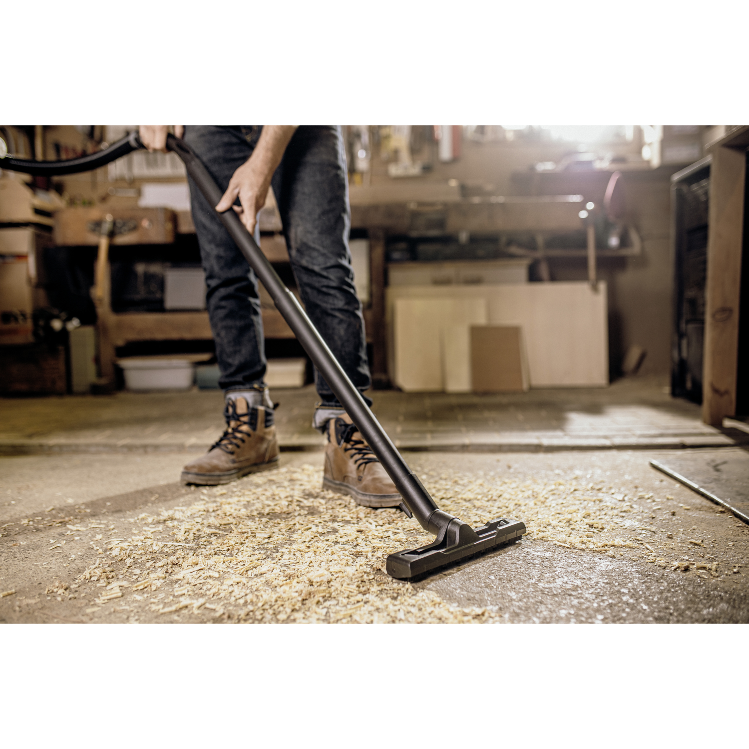 Man vacuums wood shavings on a workshop floor.