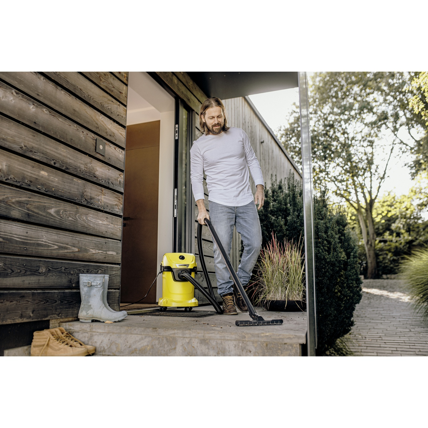Man vacuums doorstep with yellow Kärcher wet/dry vacuum cleaner.