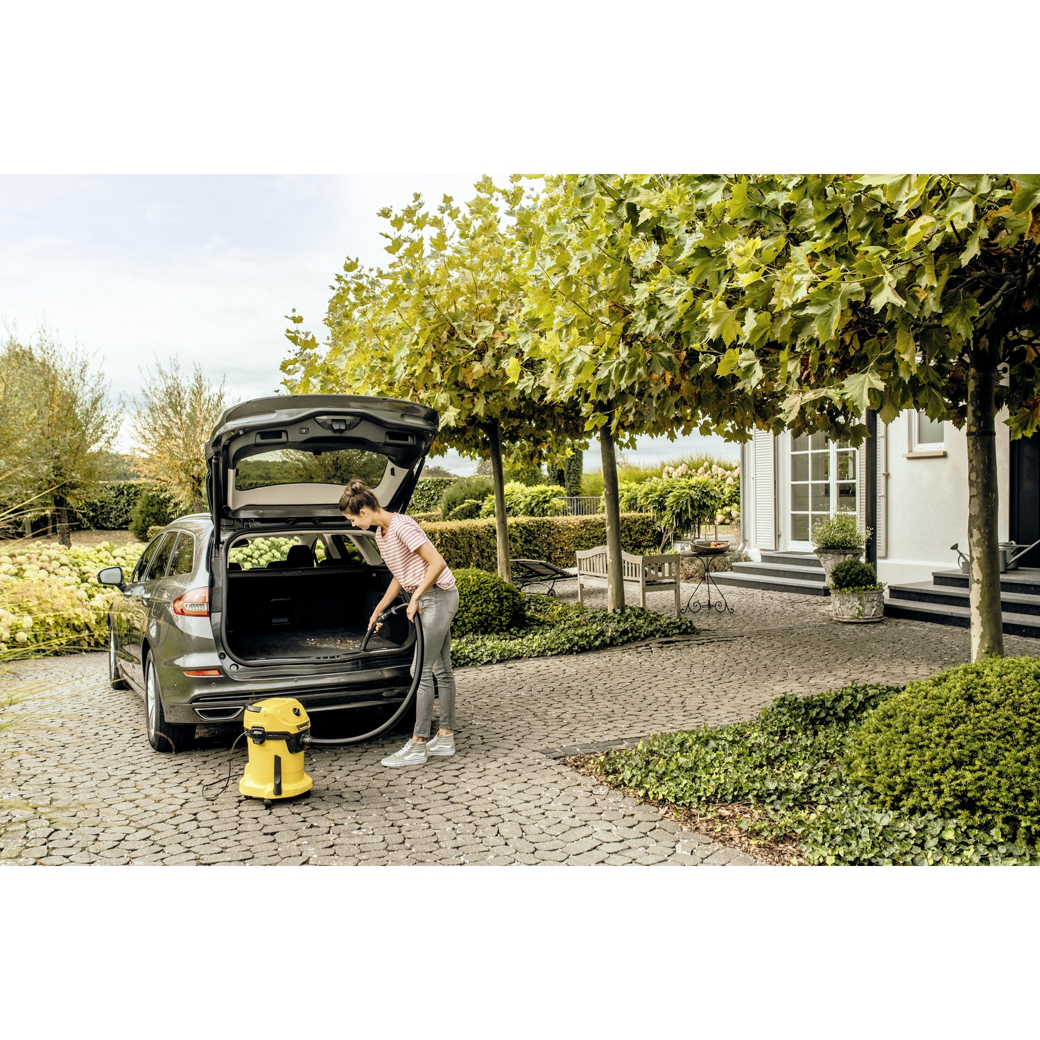 A woman vacuums the trunk of a car with a yellow vacuum cleaner.