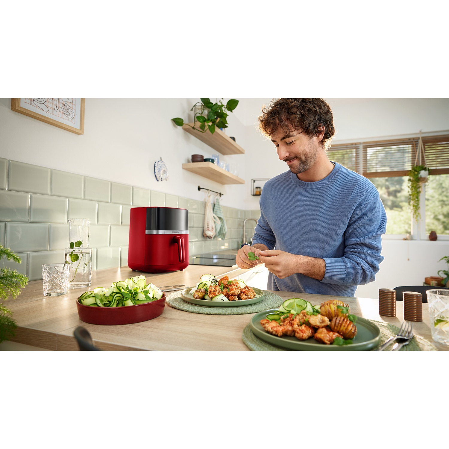 Uomo guarnisce cibo in cucina con friggitrice rossa e insalata.