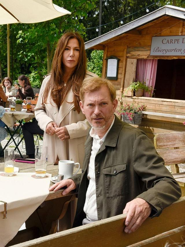 Ein Mann und eine Frau sitzen an einem Tisch im Freien vor einem Biergartenhäuschen.
