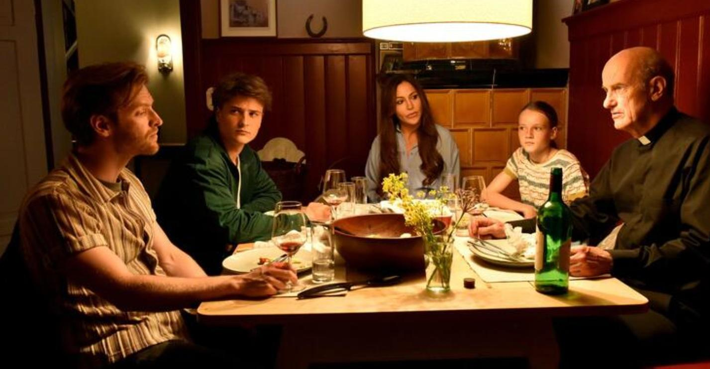 Fünf Personen sitzen an einem Tisch bei Kerzenlicht bei einem Abendessen.