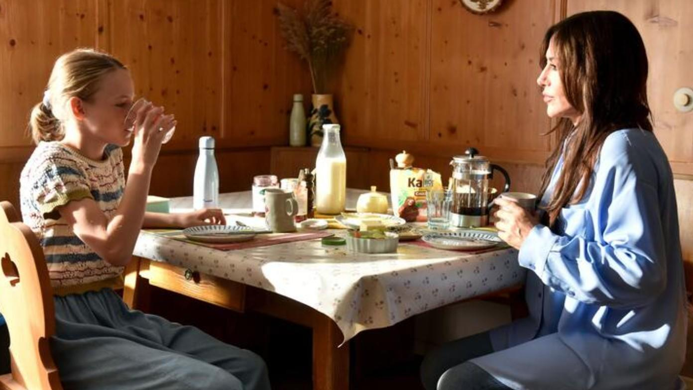 Mutter und Tochter beim Frühstück am Holztisch mit vielen Lebensmitteln.