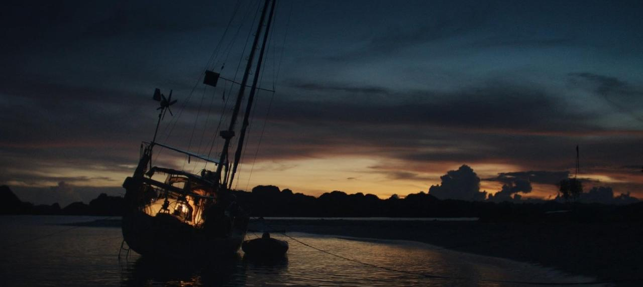 Ein Segelschiff liegt im Wasser bei Sonnenuntergang mit dramatischen Wolken am Himmel.