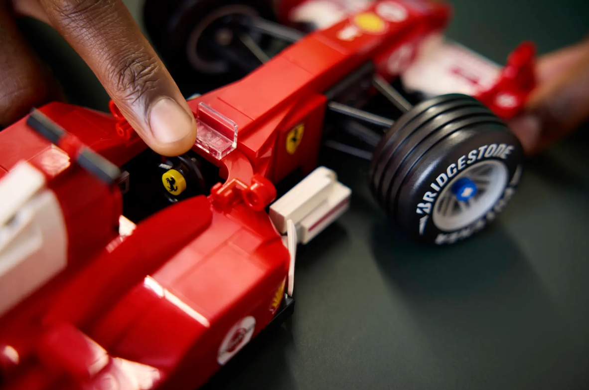 Eine Hand berührt einen roten Lego-Ferrari. Die Reifen sind schwarz mit Bridgestone-Aufschrift.
