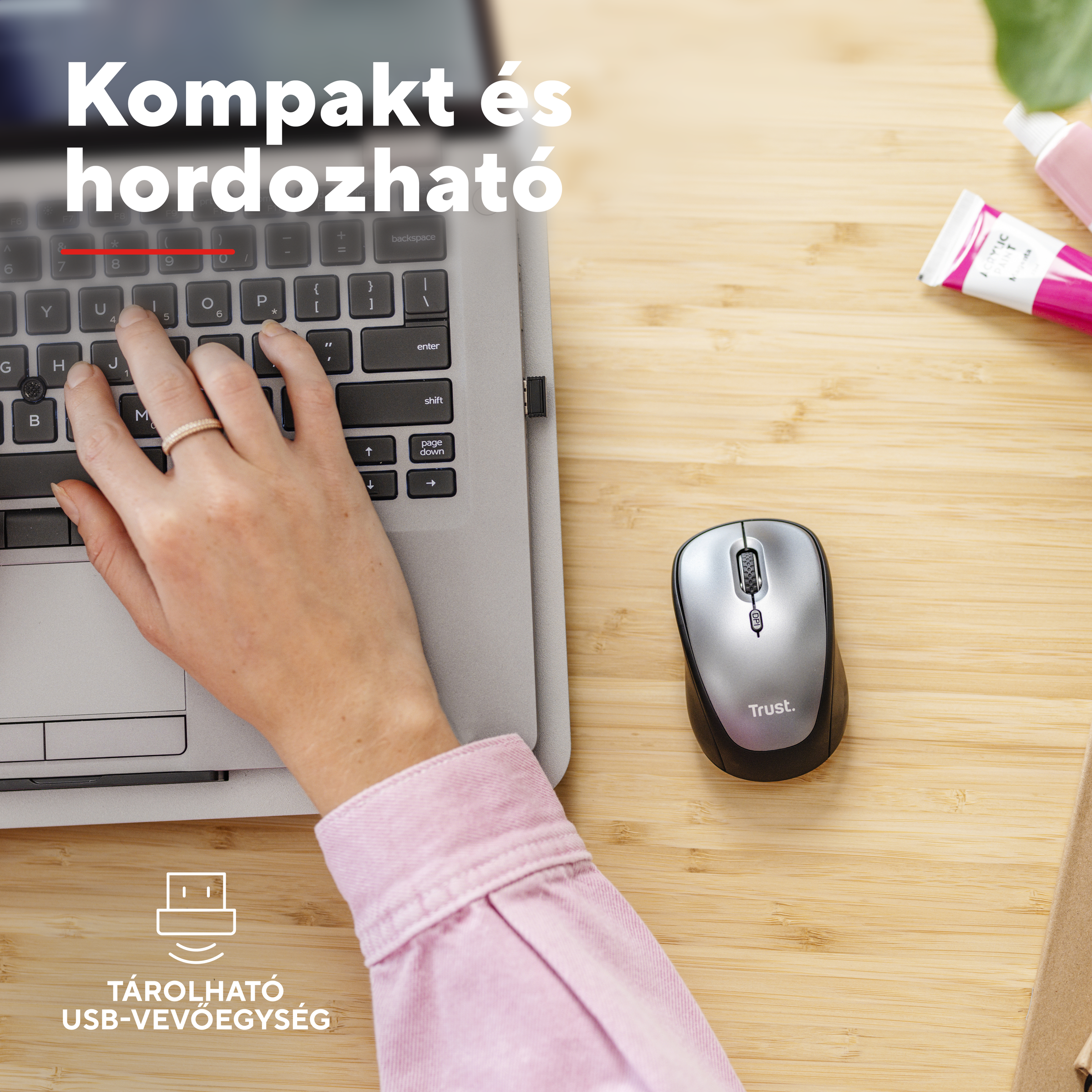 Egy kéz laptop billentyűzetén gépel, egér és festékes tubusok mellett.
