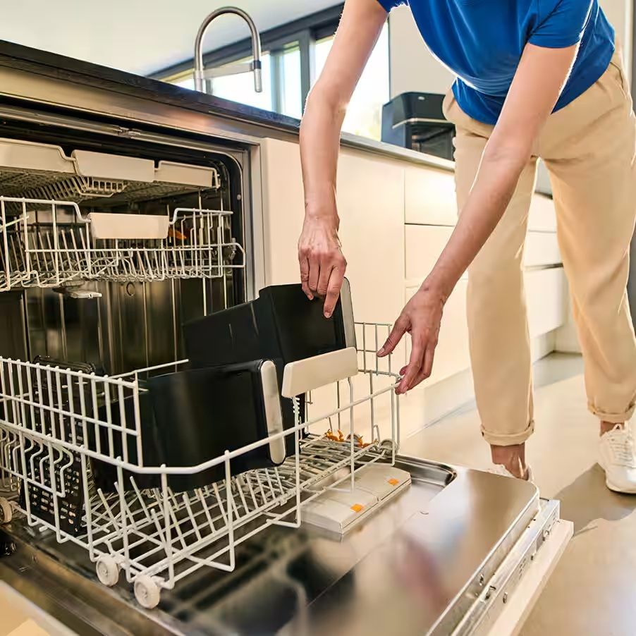 Osoba wkłada czarne kosze do otwartej zmywarki.
