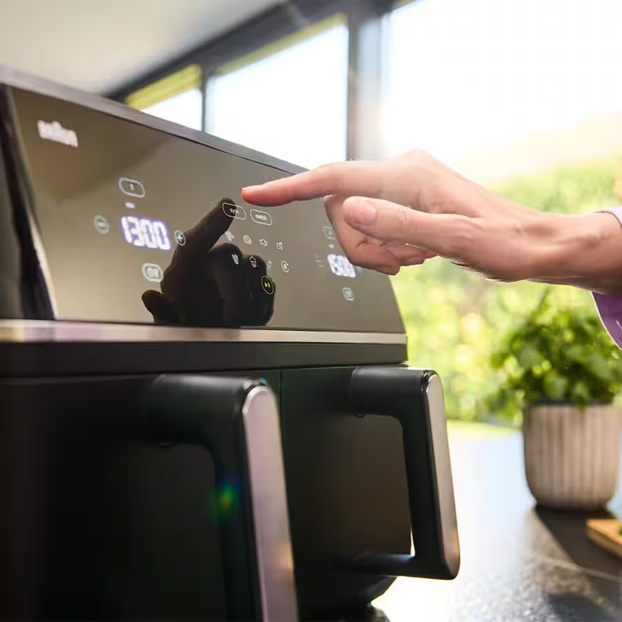 Ręka obsługuje cyfrowy ekran dotykowy czarnej frytkownicy beztłuszczowej.