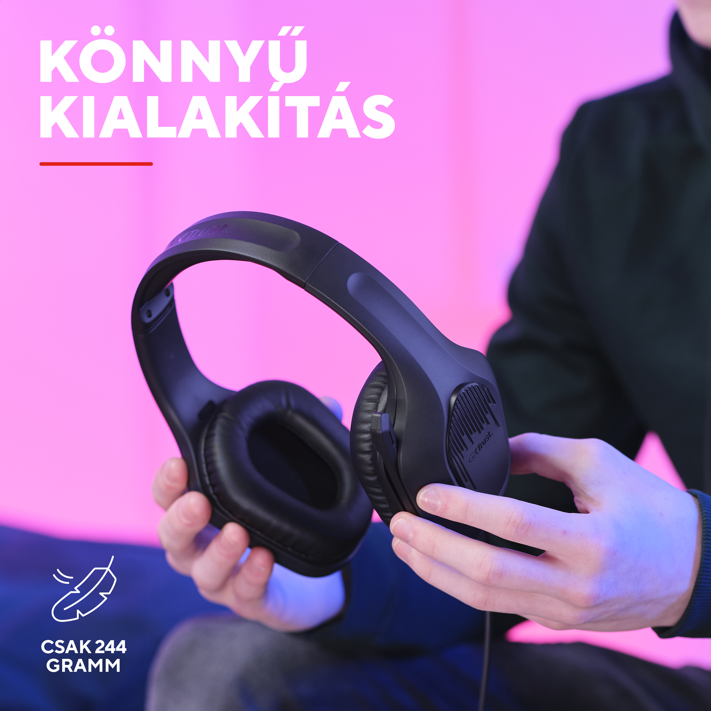 Személy fekete, puha fülpárnás fejhallgatót tart rózsaszín háttér előtt.
