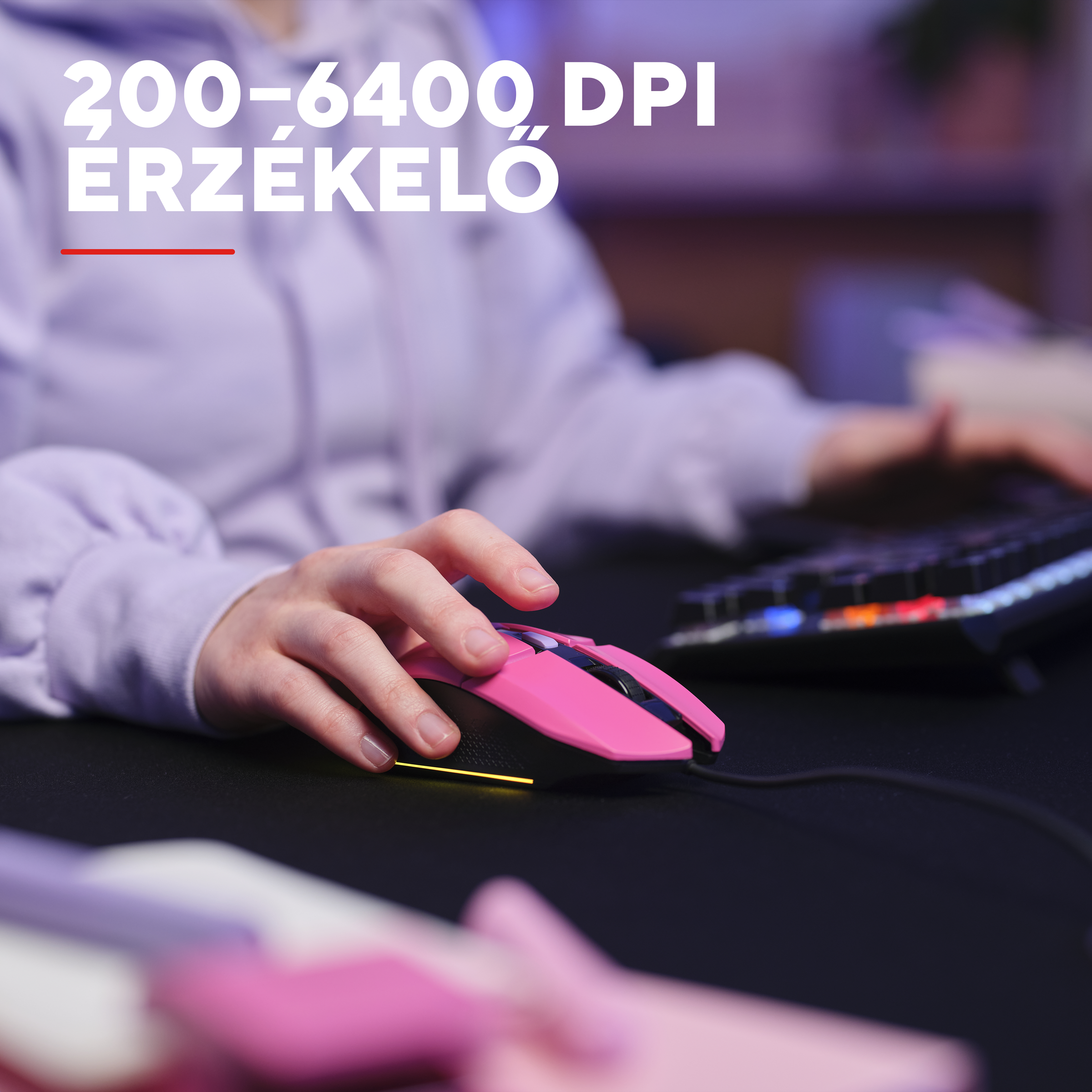 Egy kéz rózsaszín gamer egeret használ, a háttérben billentyűzet.