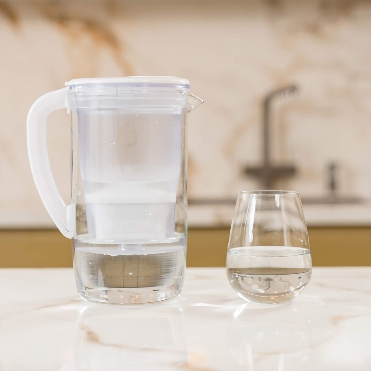 Dzbanek filtrujący wodę i szklanka wody na marmurowej powierzchni.
