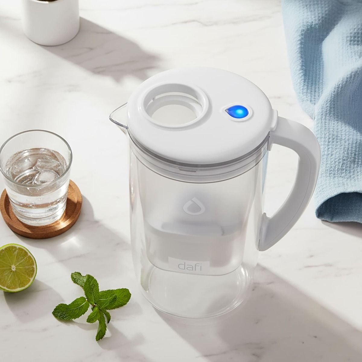 Biały dzbanek filtrujący wodę z niebieskim światłem obok szklanki wody.