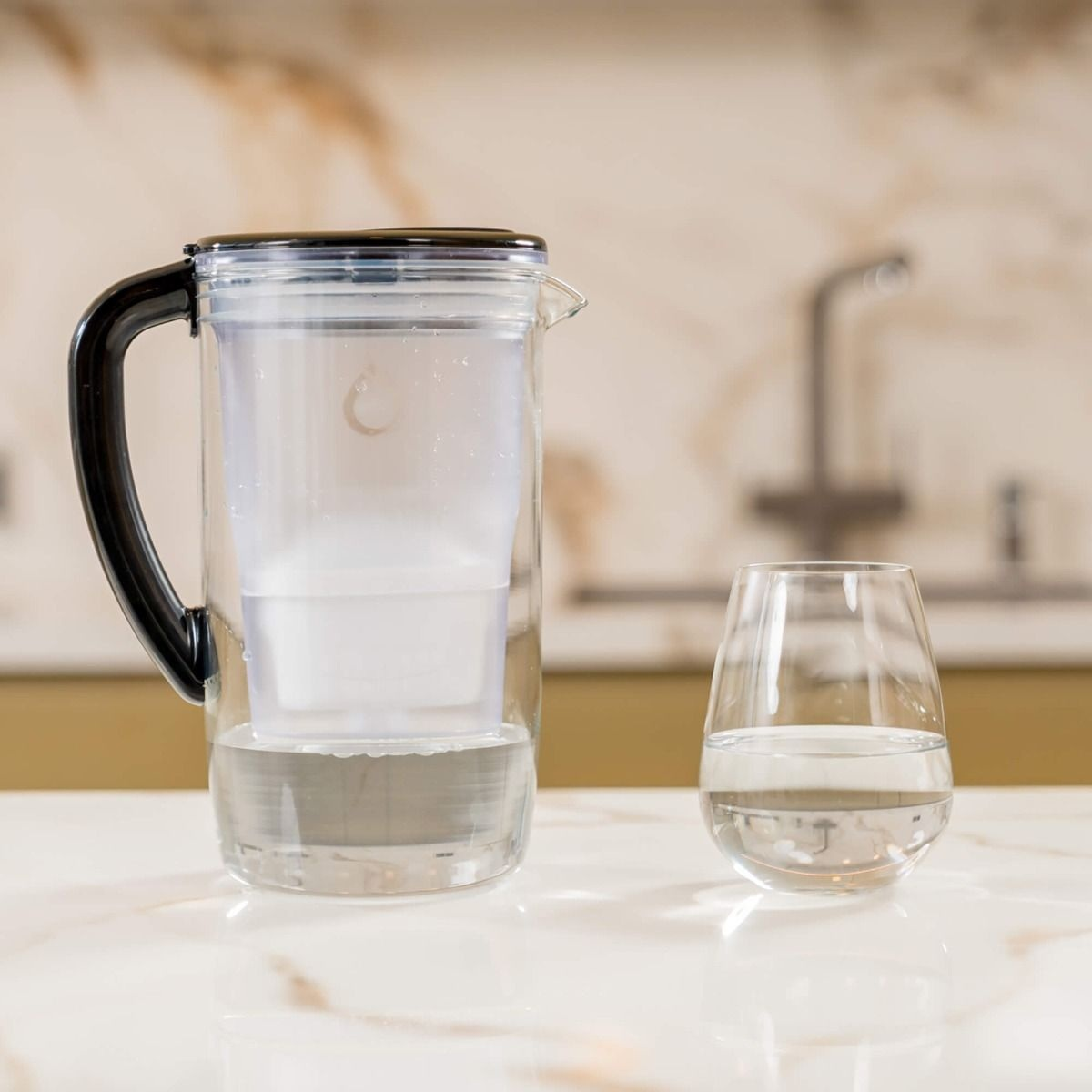 Dzbanek na wodę i szklanka z wodą na marmurowym stole.