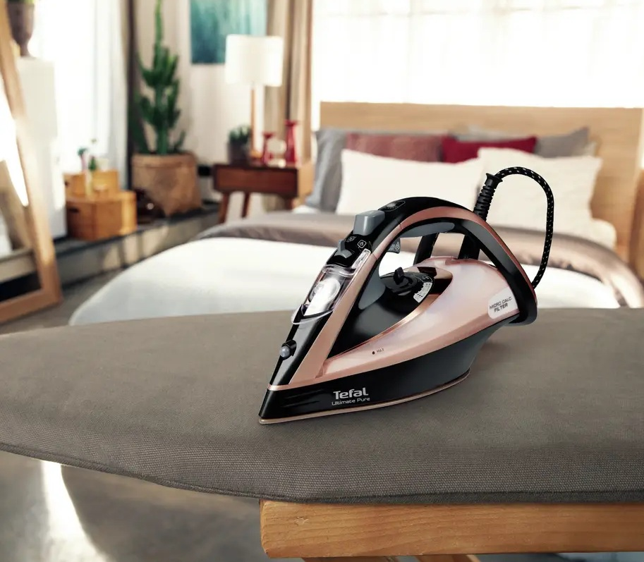 Czarno-różowo-złote żelazko stoi na desce do prasowania w sypialni.