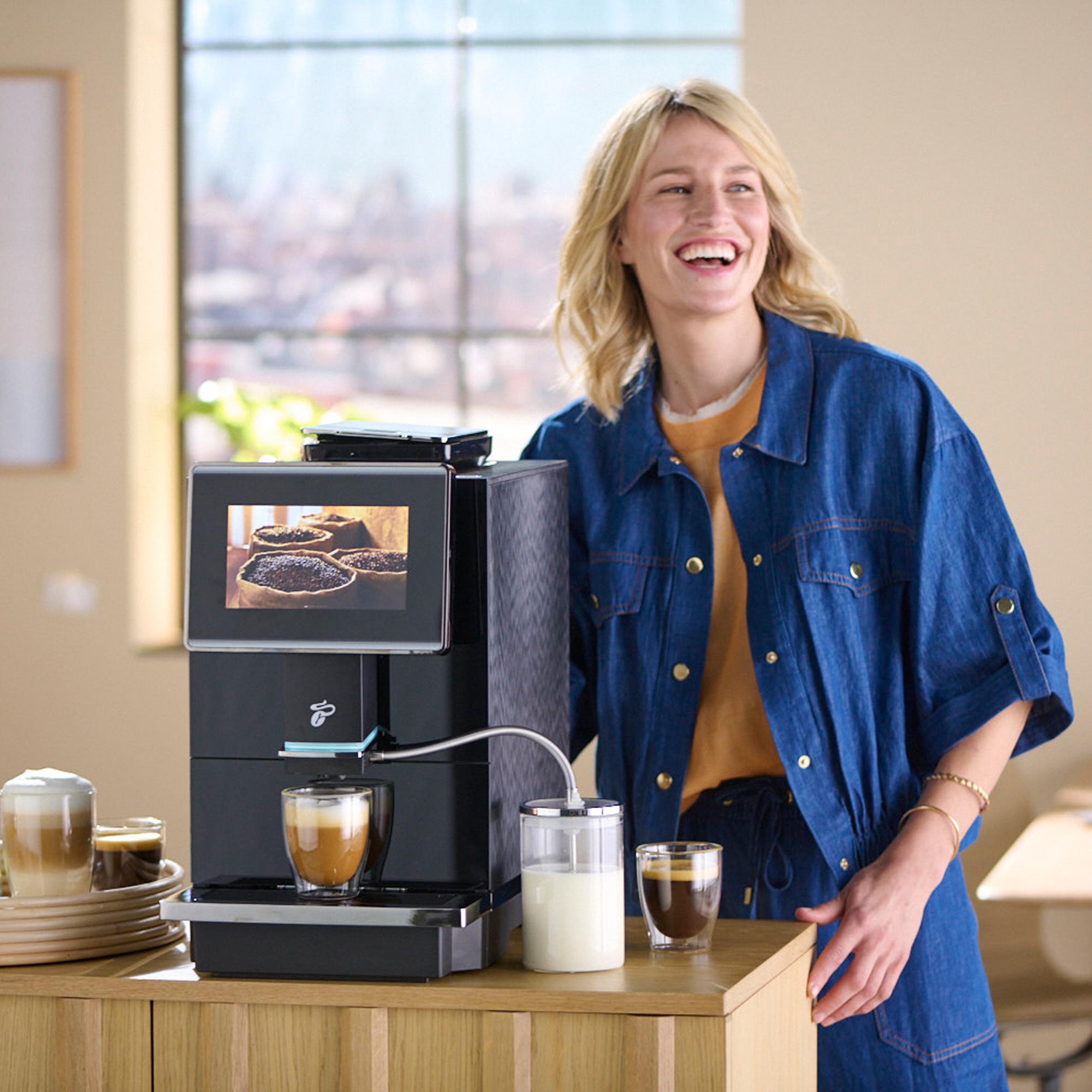 Eine Frau steht neben einer Kaffeemaschine mit Kaffee und Milch.