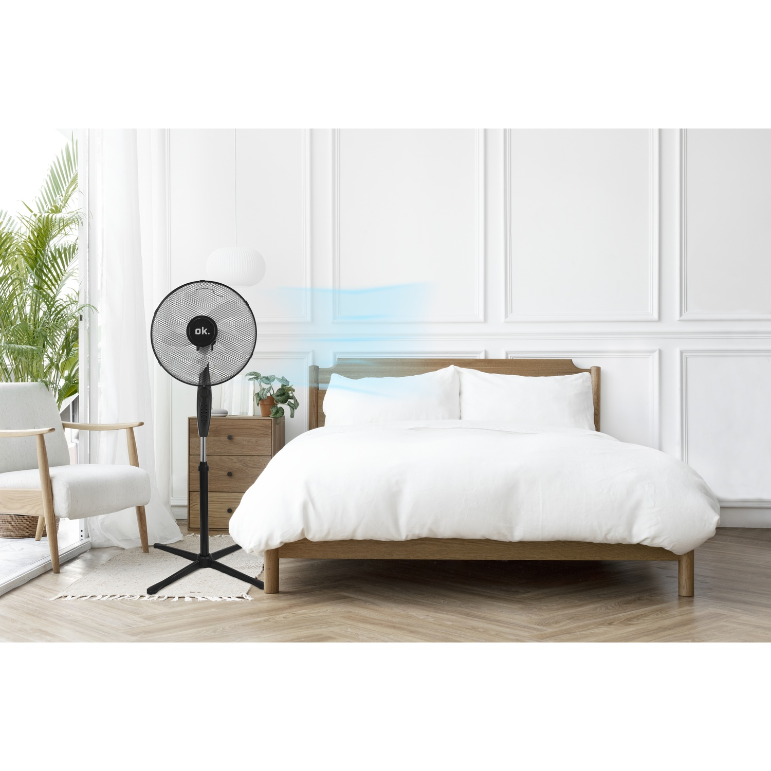 Un ventilatore da terra nero accanto a un letto con biancheria da letto bianca.