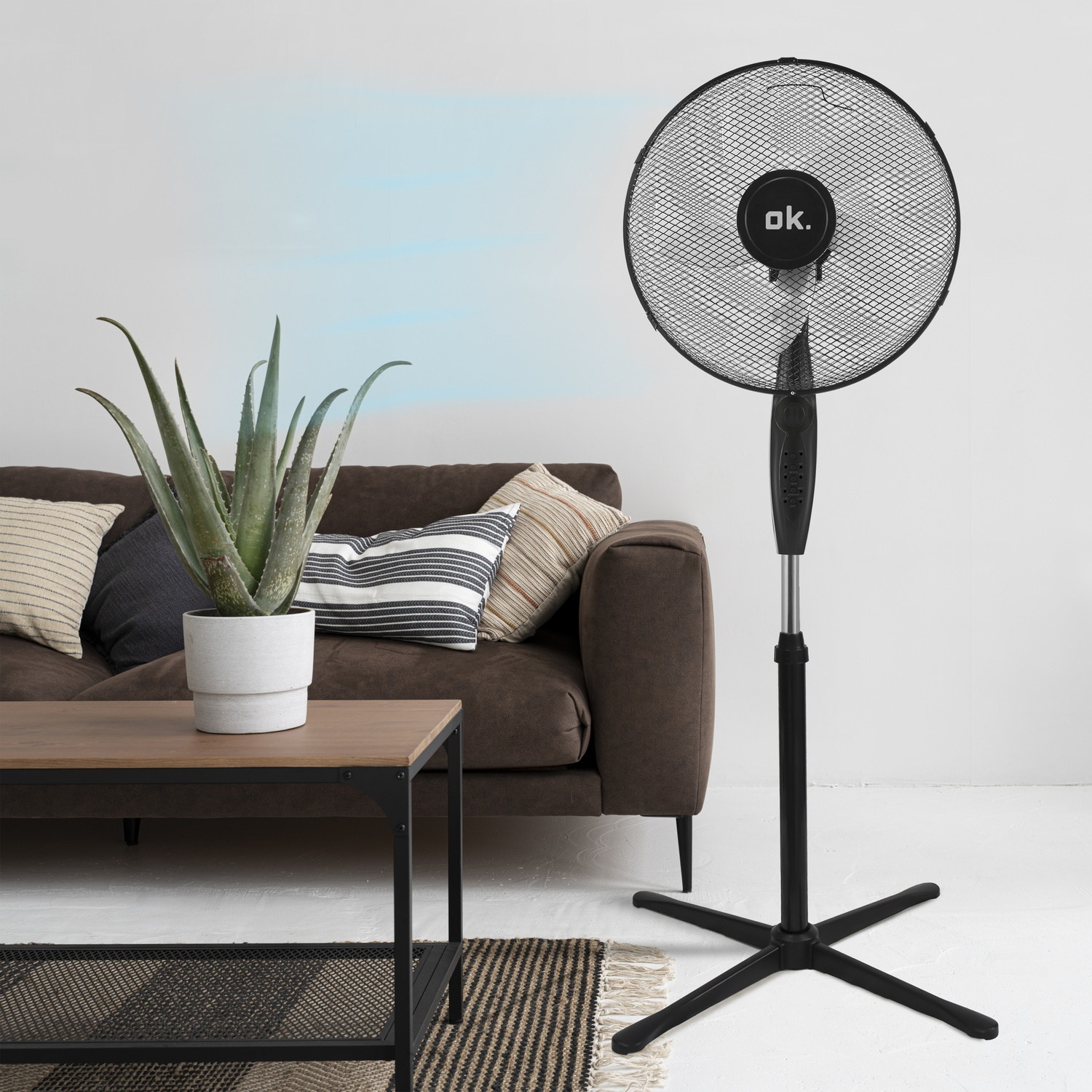 Un ventilatore da terra nero è accanto a un divano marrone con cuscini.