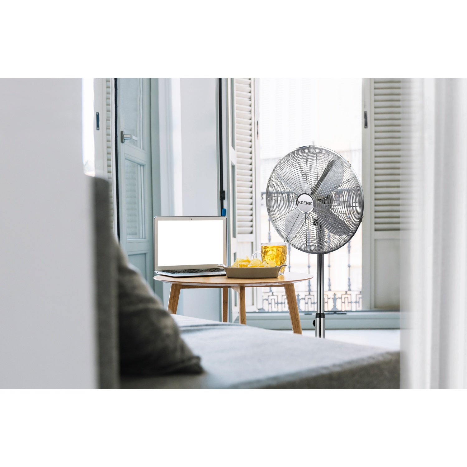 Un ventilatore accanto a un tavolo con laptop, patatine e bevanda.