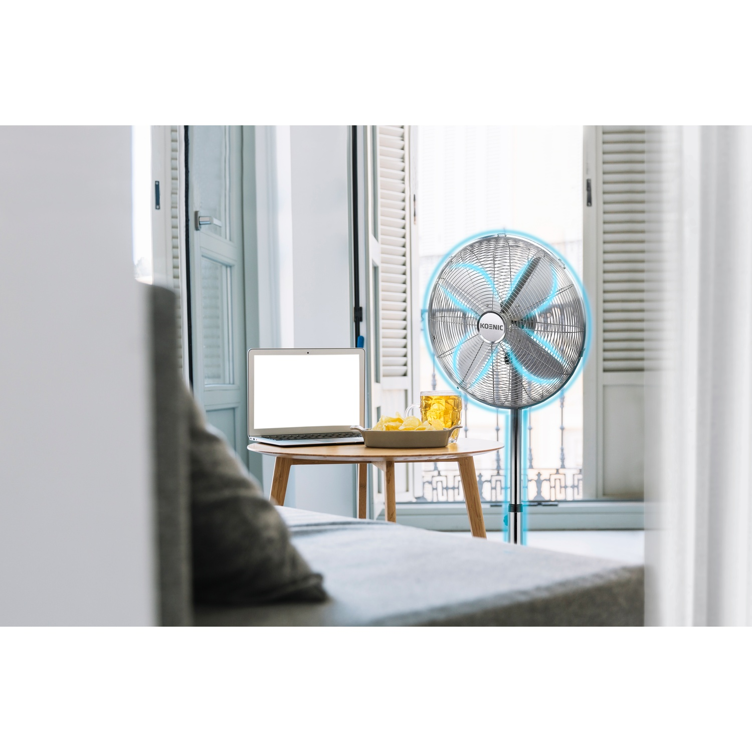 Un ventilatore accanto a un tavolo con laptop e bevanda.