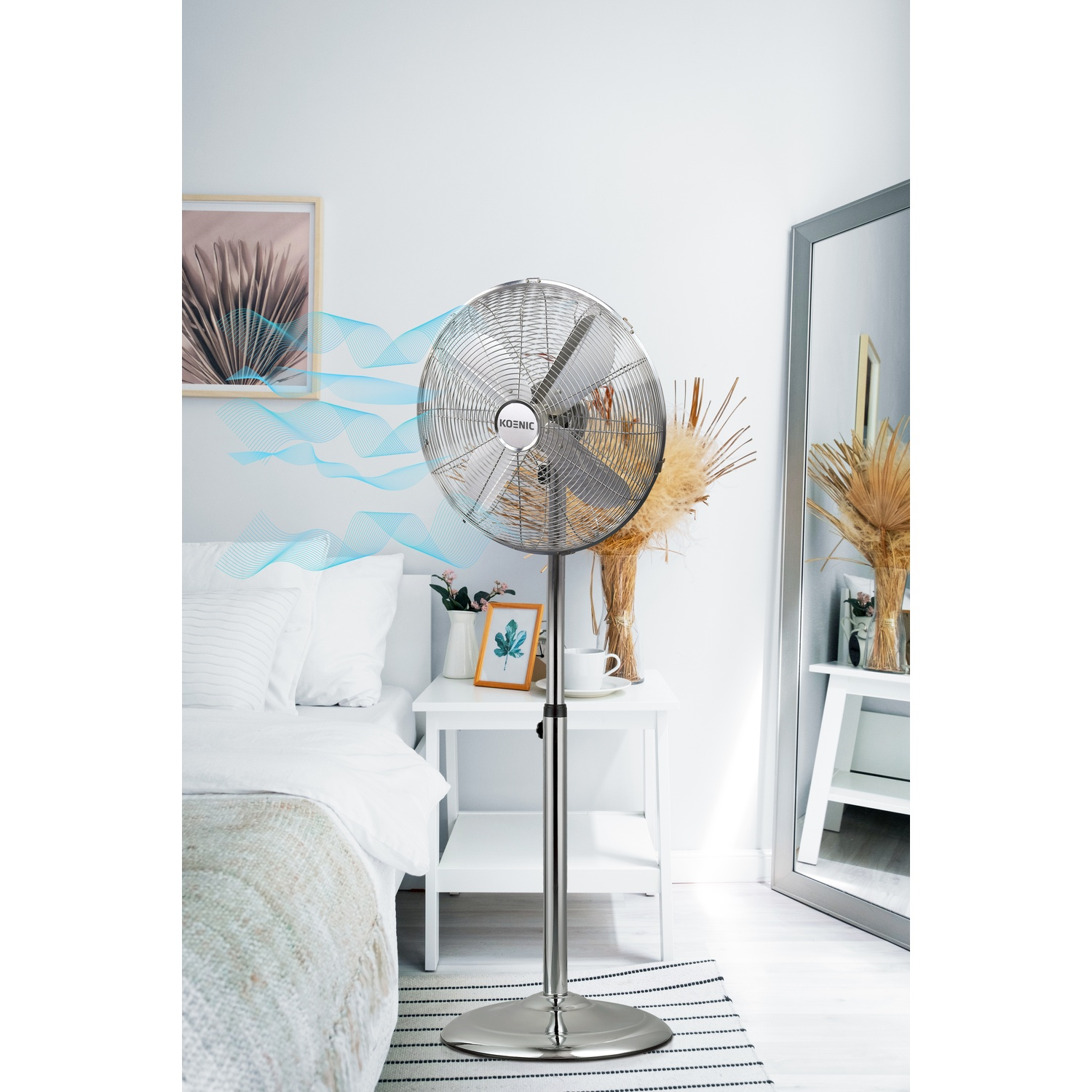 Un ventilatore da terra argentato si trova in una camera da letto accanto a un letto.