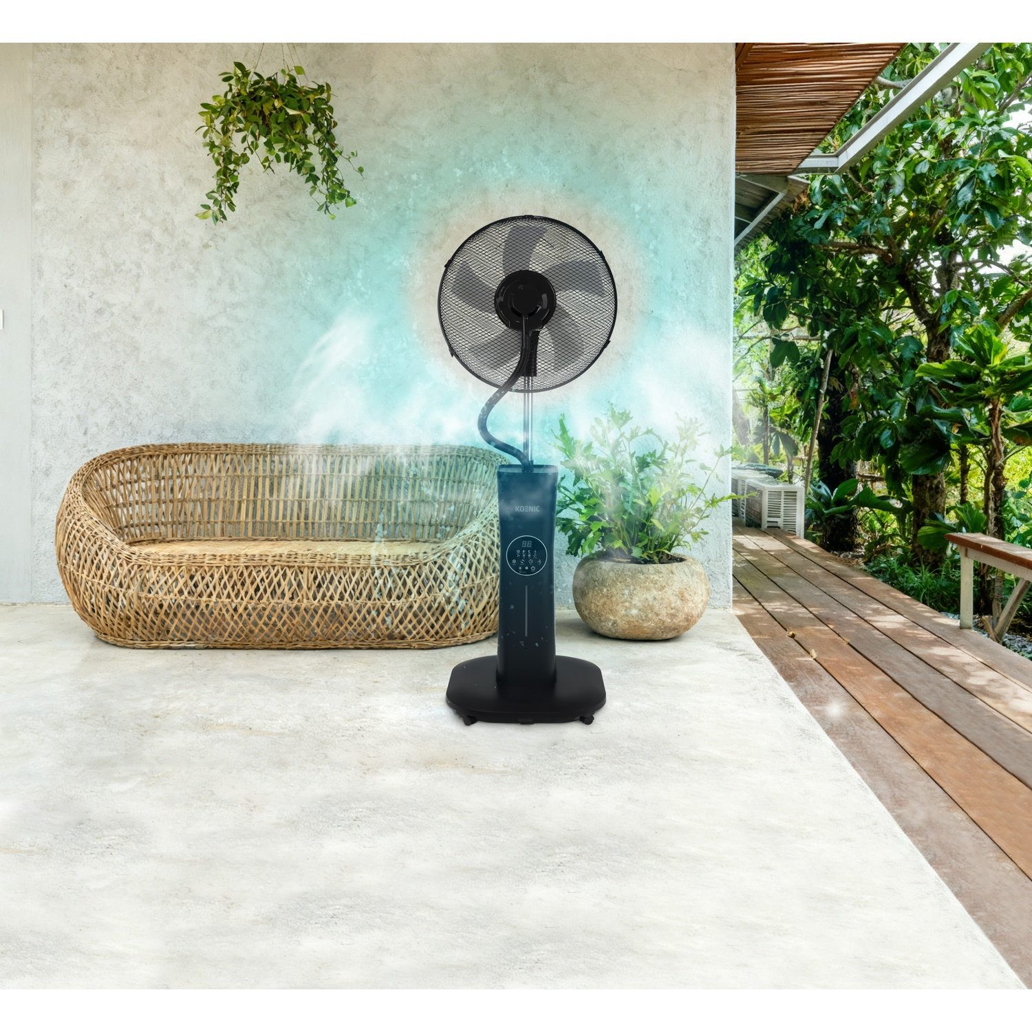 Un ventilatore nebulizzatore nero spruzza acqua davanti a una poltrona in vimini e piante su un patio.