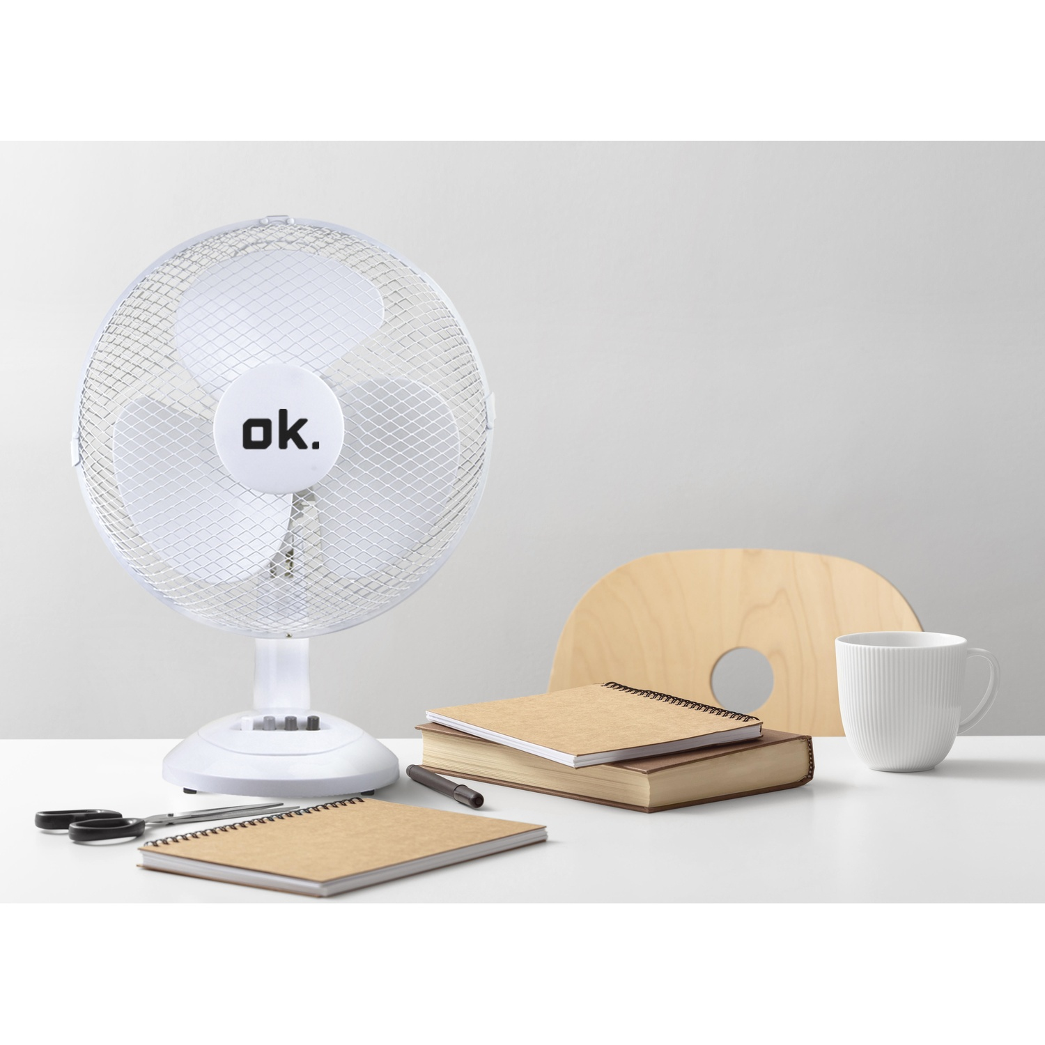 Ventilatore da tavolo bianco accanto a libri, quaderni, tazza e forbici.