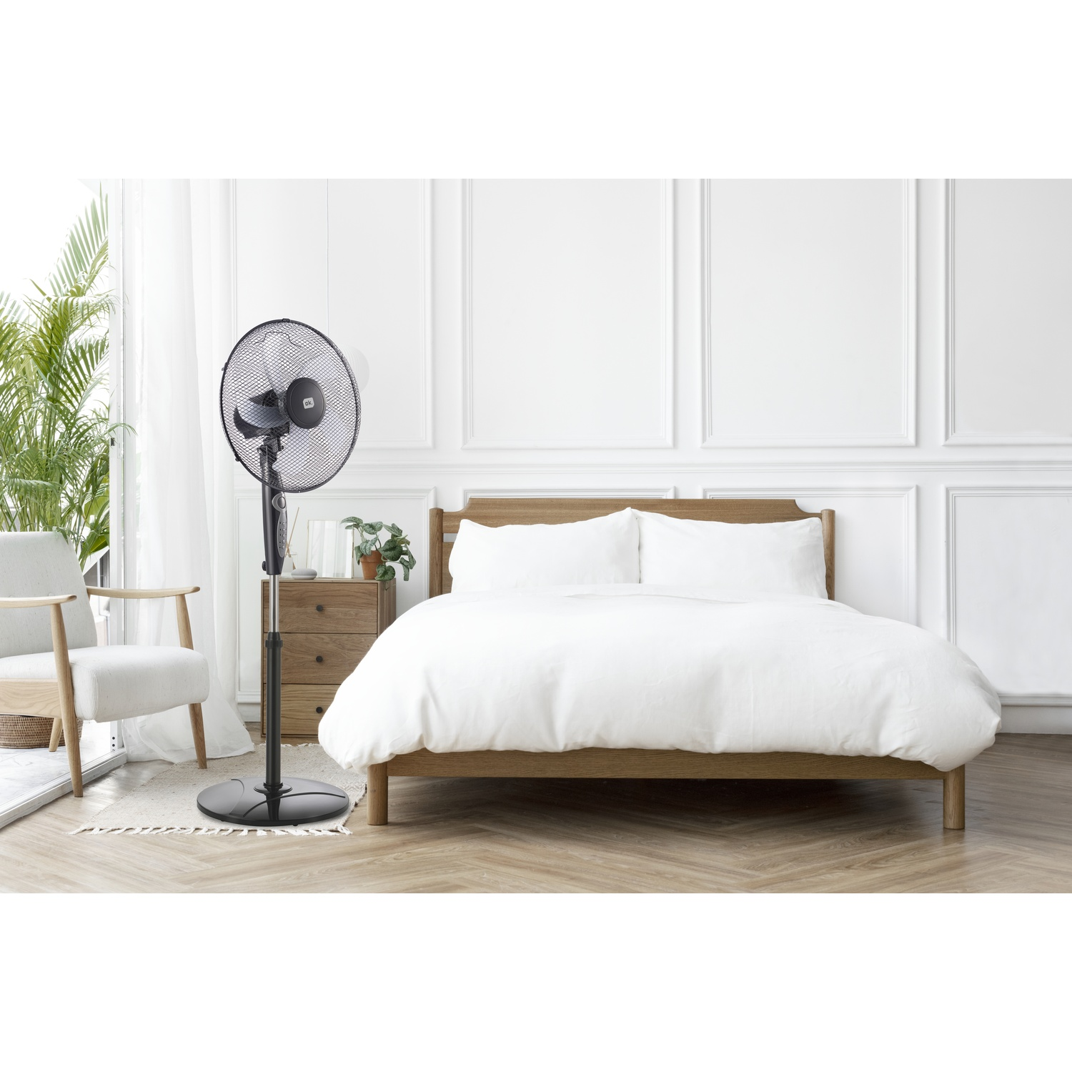 Un ventilatore a piantana nero accanto a un letto in legno con biancheria bianca.