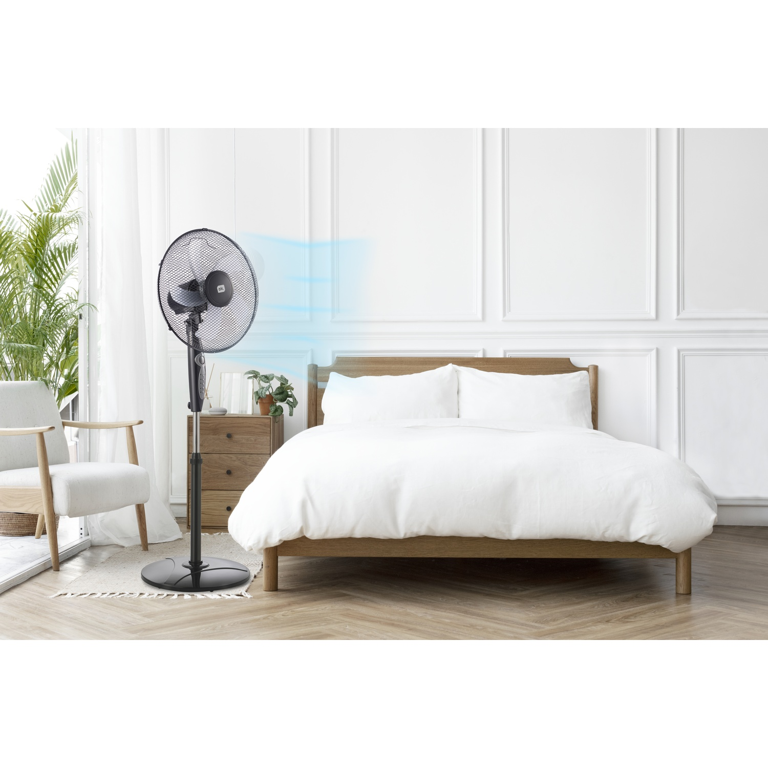 Un ventilatore a piantana nero soffia aria verso un letto bianco in una camera da letto.