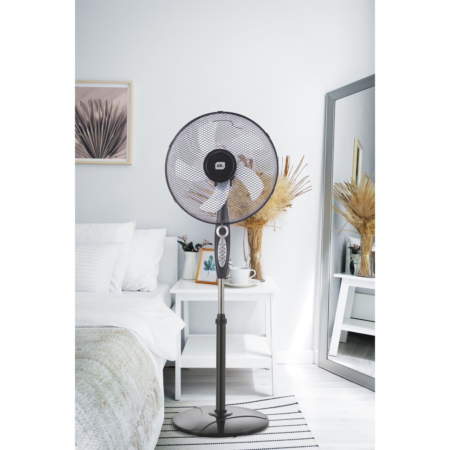 Un ventilatore a piantana è accanto a un letto in una camera da letto.