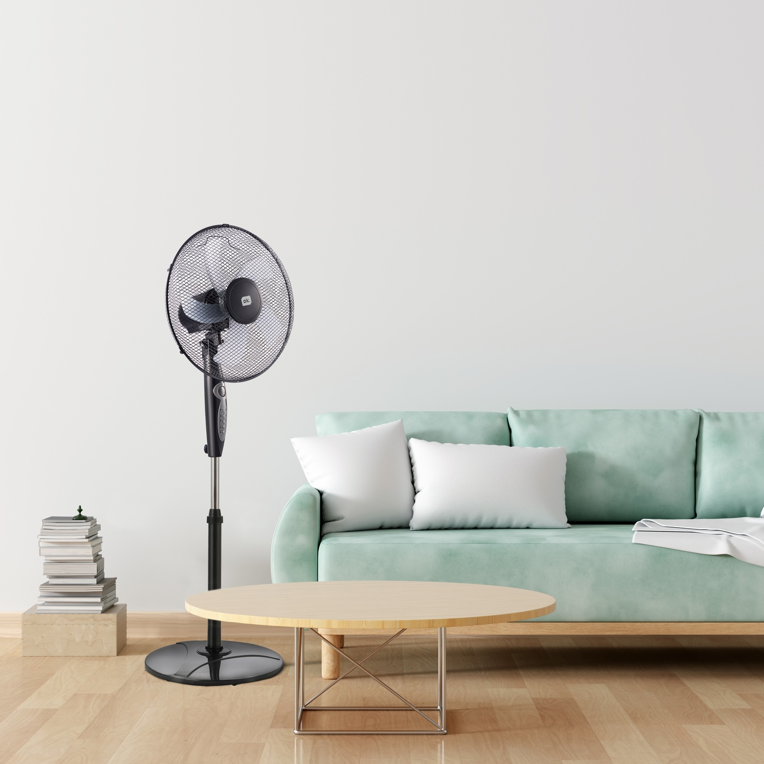 Un ventilatore a piantana è accanto a una pila di libri e un divano.