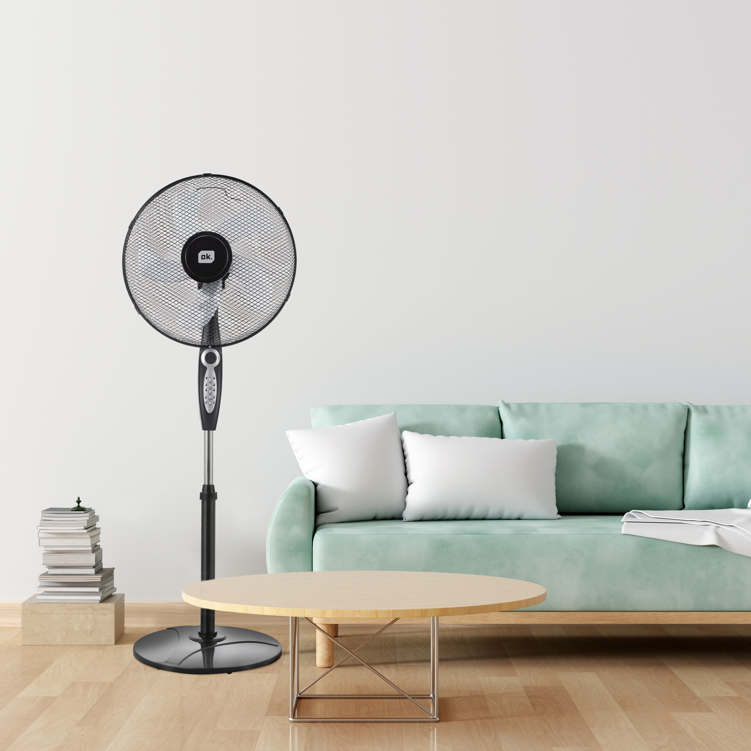 Un ventilatore nero da terra accanto a un divano verde chiaro con cuscini bianchi.